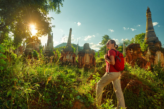 female traveler with backpack walking and looks at sunset among ancient Buddhist stupas. Mayanmar (Birma)