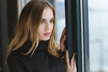 Fototapeta premium Attractive pensive young woman looking out of the window