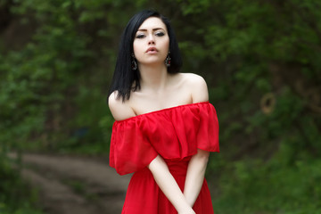 Portrait of a beautiful young girl with green eyes and bare shoulders, in a red dress on a green background summer nature.