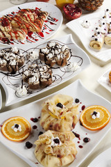 Different kinds of pancakes stuffed with various fillings and decorations, served on a table in white plates next to fresh fruit.