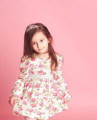 Little girl 4-5 year old posing in room over pink. Wearing trendy floral dress. 
