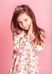 Smiling kid girl 4-5 year old wearing trendy dress with floral pattern posing over pink. Looking at camera