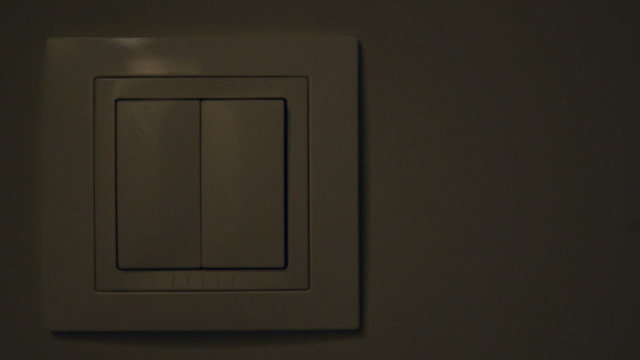 Womans hand with finger on light switch.
