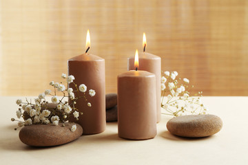 Fototapeta na wymiar Beautiful composition of alight candles with pebbles and flowers on the table