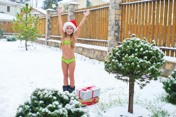 Brave child girl in bikini stay under snow fall in Santa Hat rea
