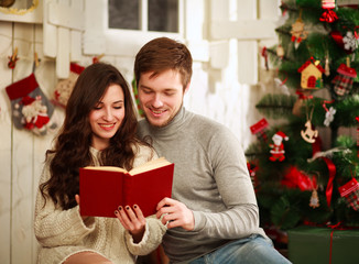 Happy couple reading book on background Christmas decorations