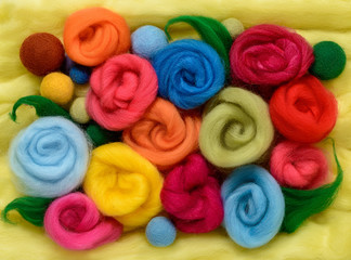 Multi-colored stylized roses and beads made of wool for felting. Situated on the bright green merino wool..