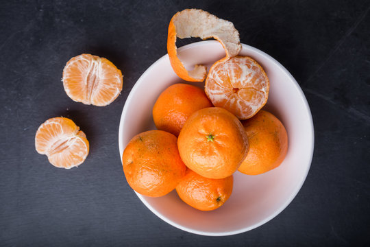 Organic mandarin oranges in white bowl on black table