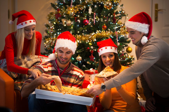 Four young friends sharing pizza while celebrating Christmas or New Year's eve at home