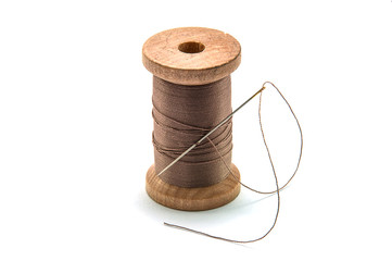 Isolated wooden spool of brown thread with a needle