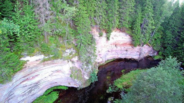 The Taevaskoda sandstone on the side of the mountain. Theres green trees on the forest surrounding the river