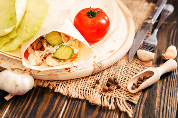 
shaverma , roll, pita bread with fried chicken, cabbage , tomatoes, cucumbers , carrots , garlic , mayonnaise and spices on a wooden background