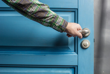 man holding on to by its metal handle in the open wooden door blue
