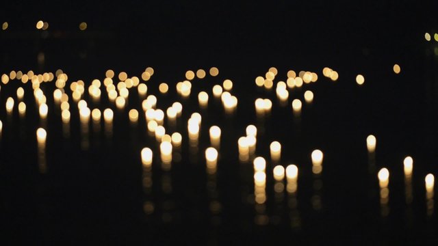 Burning candles float on water during Loi Khrathong celebration in Sukhothai, Thailand. In and out of focus.