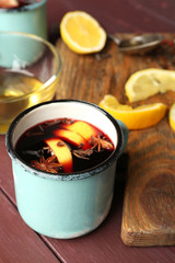 Mulled wine in a mug with citruses on wooden background, close up