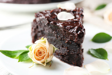Piece of chocolate cake decorated with flowers on white wooden table