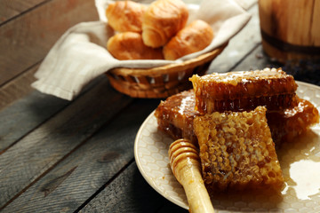 Honeycombs on plate, hot buns in basket on wooden background