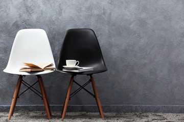 Stylish conception with white and black chairs on grey background