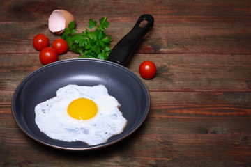 Pan of fried egg, with cherry-tomatoes and parsley on a wooden table surface