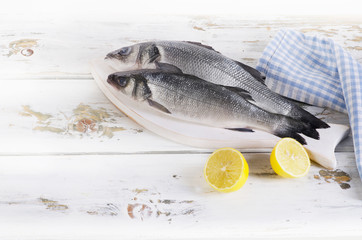 Two raw seabass with lemon on wooden background.
