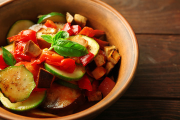 Tasty vegetarian ratatouille made of eggplants, squash, tomatoes in bowl on wooden table background