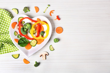Useful cut vegetables on a plate in the form of heart on wooden table top view