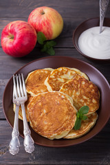 Cottage cheese pancake with apples in ceramic bowl with sour cream on a dark wooden table 