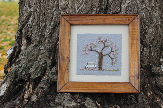 Embroidery picture bench in a garden, a blossoming tree in fallen autumn leaves