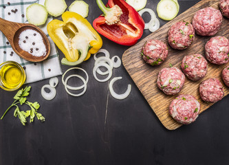 Obraz na płótnie Canvas raw meat balls with herbs and onions on a cutting board with bell peppers, butter, on wooden rustic background top view