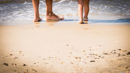 close-up of mother and son's feet on the sand approaching the sea in a sunny day - conceptual image with copyspace