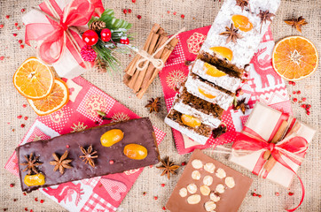 Chocolate spices cake, star anise and dried fruits, packed gifts with red tapes on sackcloth, canvas. Sweet frame. Top view