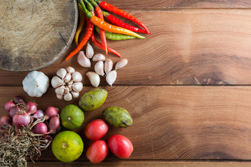 Thailand Food Ingredients: Tomatoes, peppers, garlic, shallots, lemon, olive with a mortar on a wooden floor.