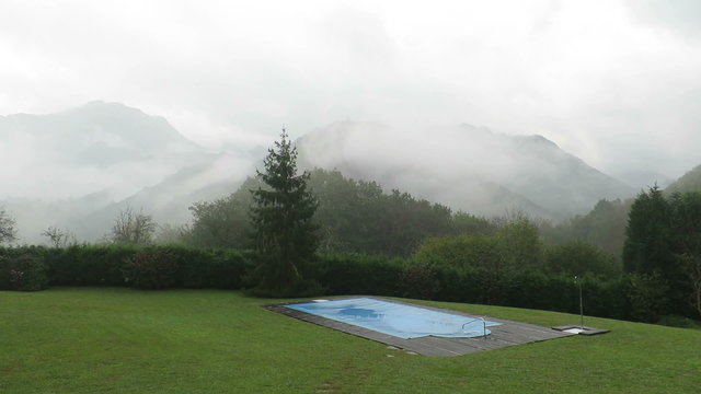 landscape of green meadow with swimming pool closed and covered with blue tarp in winter rounded by mountains with fog and rain and clouds running in Nature in Asturias Spain Europe