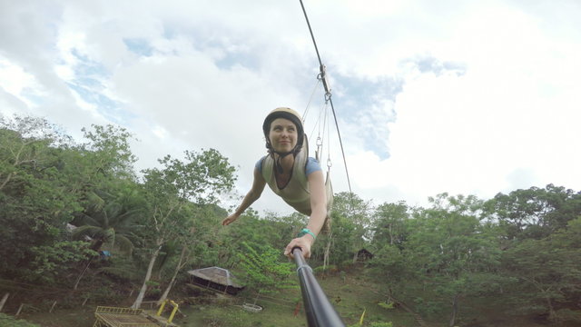 Brunette girl on a foefie slide over a tropical river selfiestick perspective.
