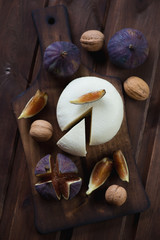 Cheese with figs and walnuts on a dark rustic wooden surface