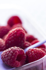 Eine Himbeere in Nahaufnahme mit mehreren HImbeeren im Hintergrund