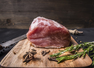 juicy piece of fresh raw pork steak on vintage cutting board with herbs and spices on wooden rustic background close up
