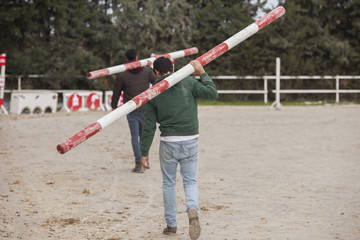 Two assistants loading obstacles poles at horse jumping competit