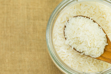 polished white rice in glass jar on gunny sack texture with copy space, top view