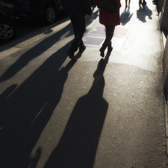 People walking in a busy city district in the late afternoon creating long shadows on the ground