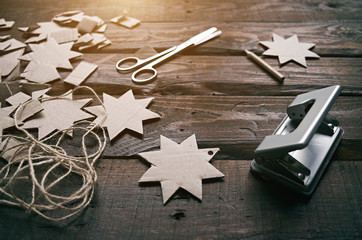 Making Christmas cardboard gifts garlands on old wooden rusty barn wood table. Winter holidays new year vintage crafting.