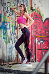 Young slim high heeled woman with long dark hair in tights and sneakers trains on the street in the summer