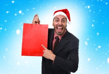 funny happy businessman in Christmas Santa hat holding red shopping bag in snow sky background