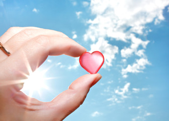 The hand holds a small semi-transparent heart in the sky