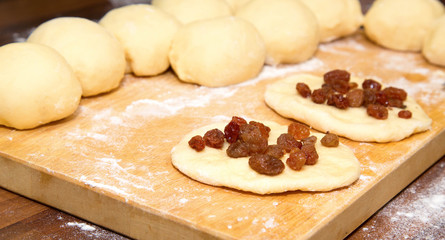 The cut dough for pies strewed with raisin on a wooden board