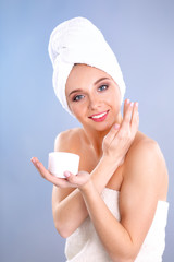 Beautiful young woman applying a creme on her face isolated on gray background