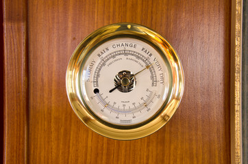 Shiny gold weather station, with barometric pressure and temperature, mounted on a wooden wall inside a boat. © Michael O'Keene