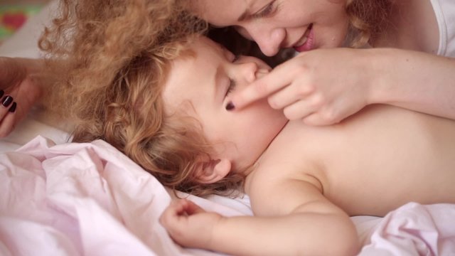 young beautiful curly girl with love looking at the baby and stroked his cheek when he sweetly asleep