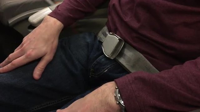 A man fasten his seat belt on an airplane.  	