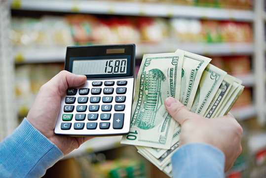 Man with dollars and calculator considers costs in store